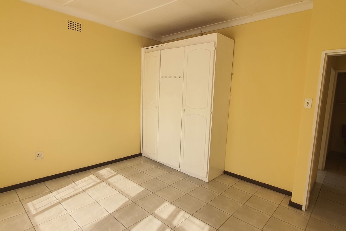 A simple bedroom featuring tiled flooring, built-in wardrobe cabinetry, and direct access to an en-suite bathroom.