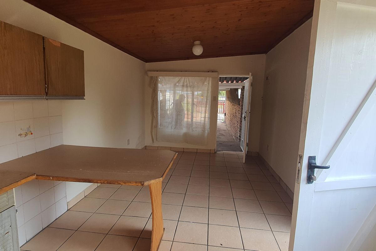 A dated kitchen area featuring wood-look cabinetry, tiled flooring, and a timber-paneled ceiling, offering a functional layout with direct access to the exterior.