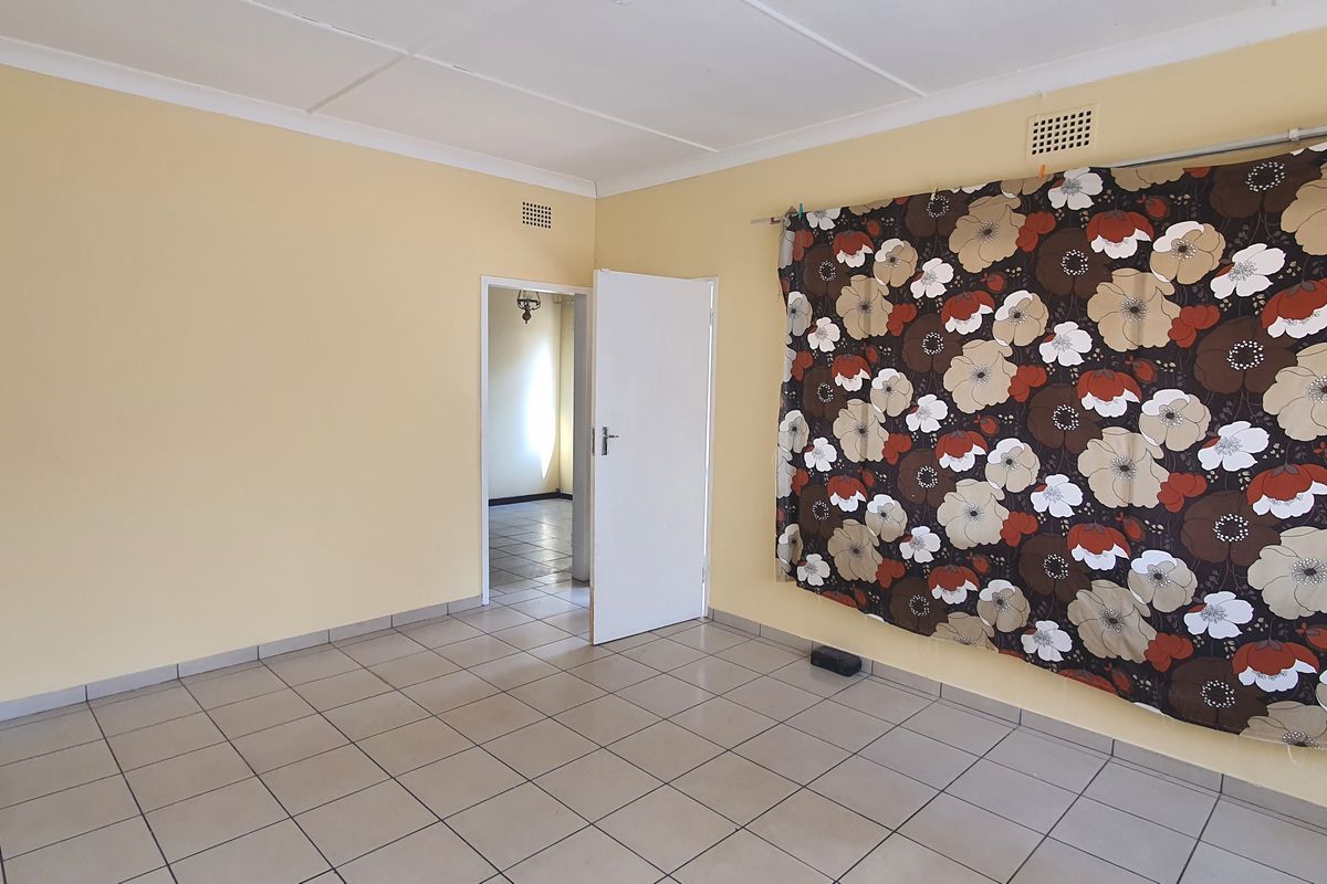 A spacious, empty living room featuring neutral tiled flooring, pale yellow walls, and a doorway leading to an adjacent room.