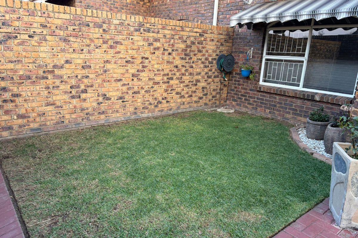 A private rear garden area featuring a small lawn, brick boundary walls, and a window with a retractable awning.