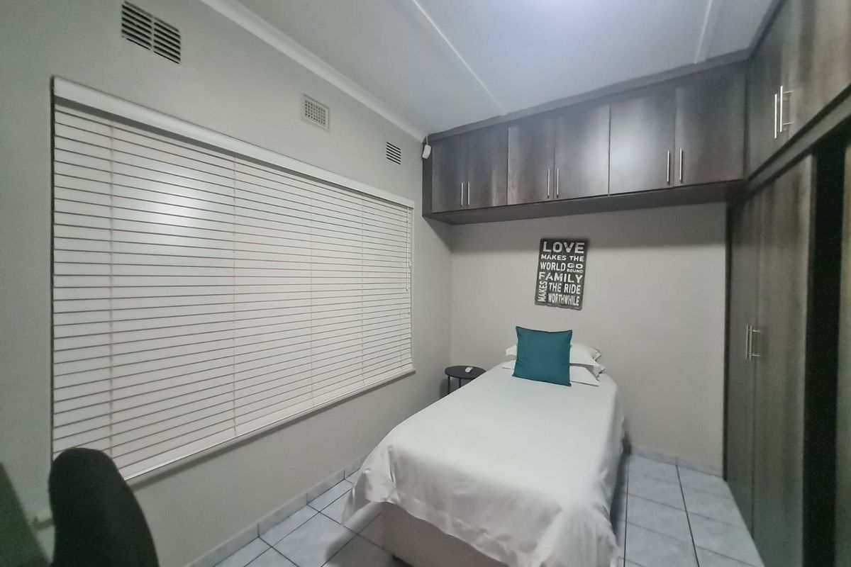 A well-maintained bedroom featuring built-in cupboards, overhead storage cabinetry, tiled flooring, and venetian blinds.