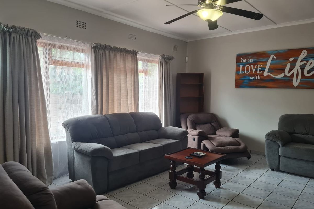 A comfortable living room featuring tiled flooring, a ceiling fan, and large windows that provide natural light.