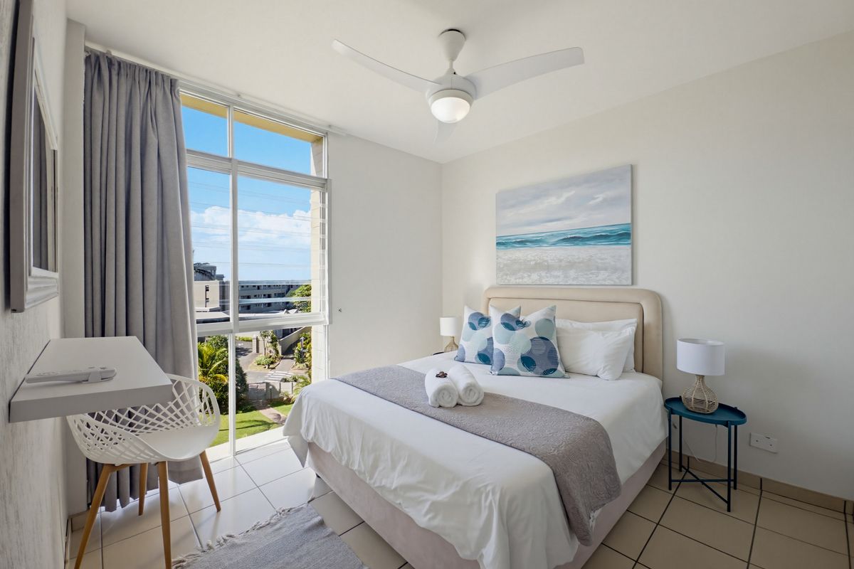 A bright bedroom featuring large windows with exterior views, a ceiling fan, and tiled flooring.