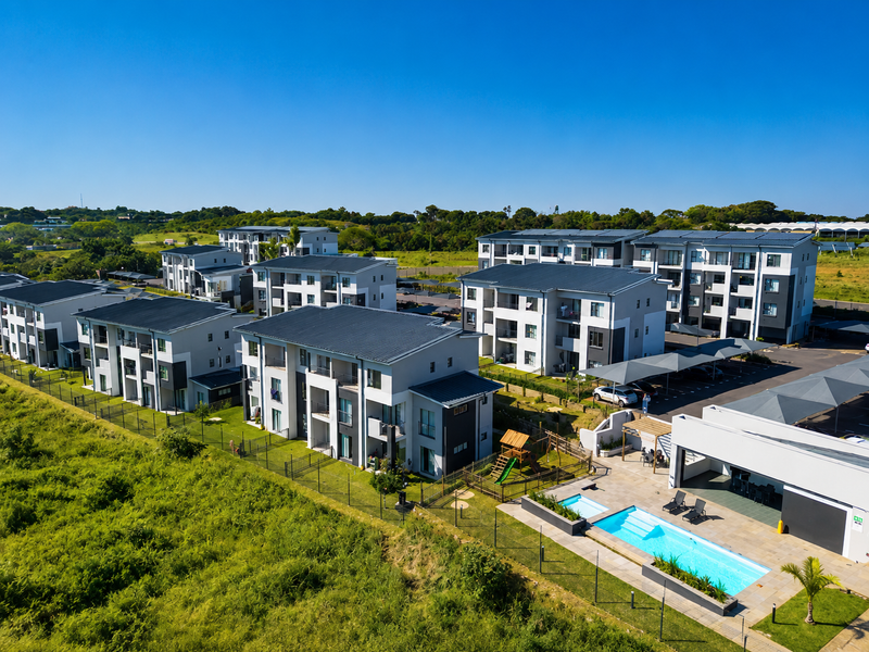 Aerial view of a modern townhouse complex featuring multiple residential blocks, a communal swimming pool, and covered parking facilities.