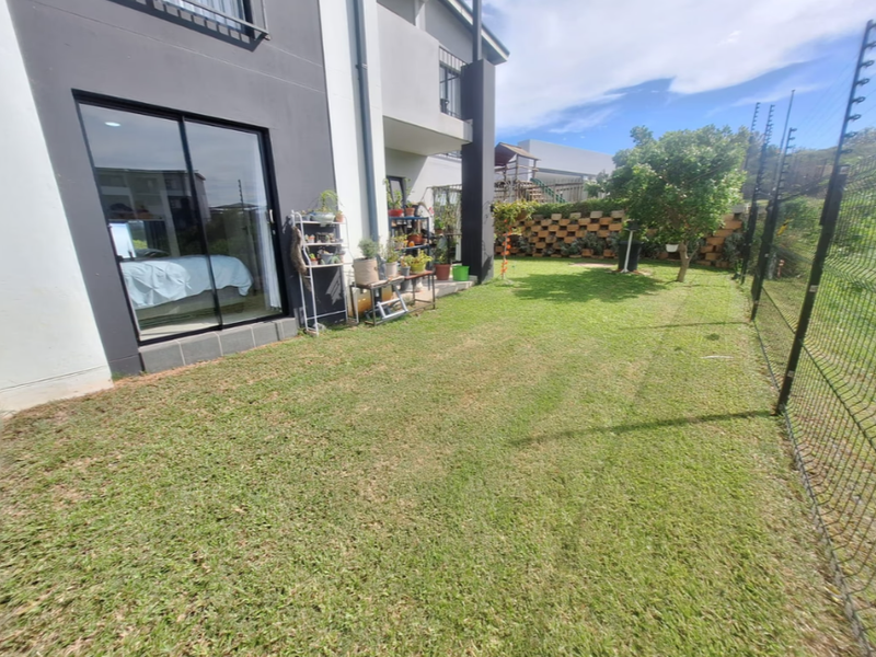 Rear garden area of the townhouse featuring a lawn, retaining wall, and secure perimeter fencing with access via a sliding glass door.