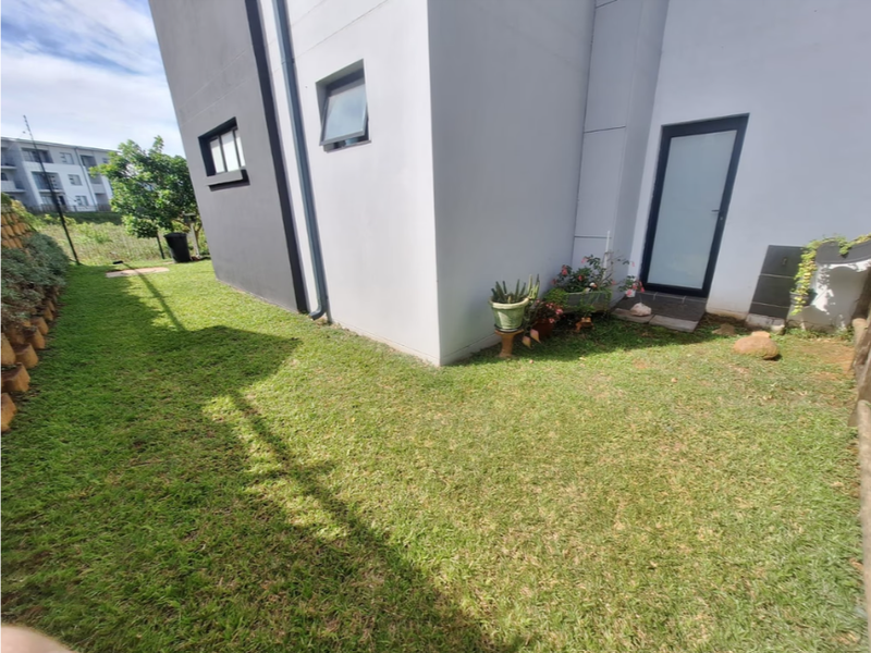 A view of the rear garden area featuring a well-maintained lawn, retaining wall, and modern exterior facade with a glass panel door.