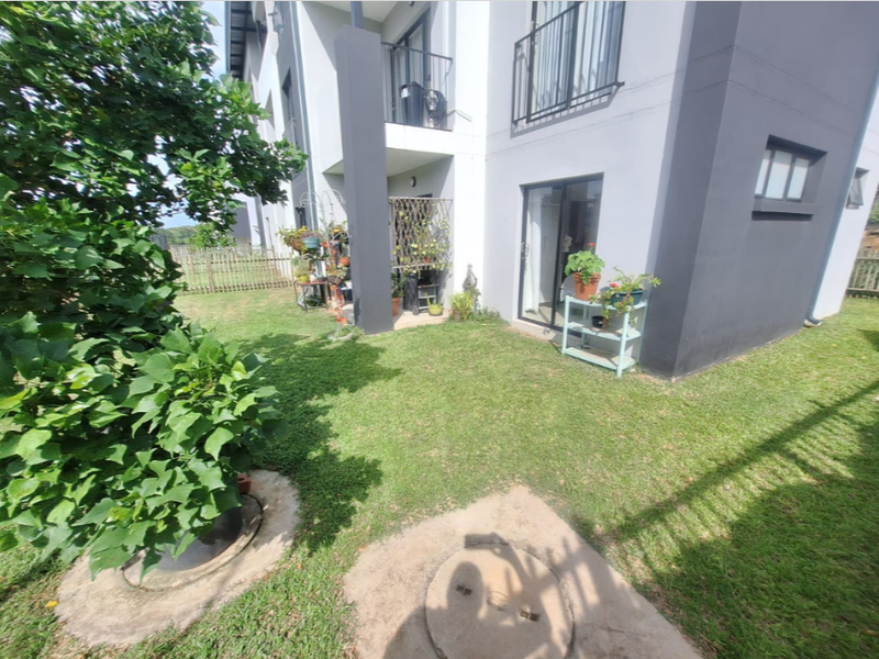 Rear view of the townhouse featuring a small private garden, a ground-floor sliding door entrance, and an upper-level balcony.