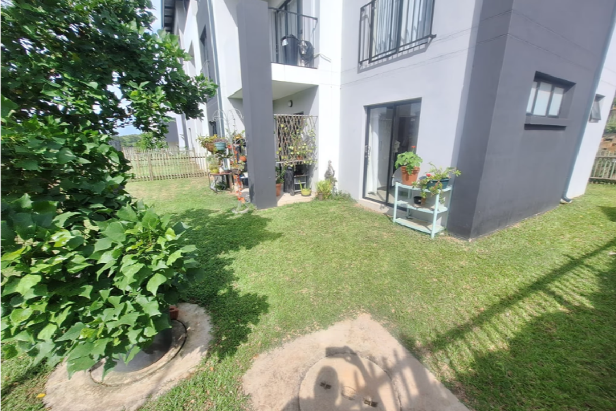 Rear view of the townhouse featuring a small private garden, a ground-floor sliding door entrance, and an upper-level balcony.