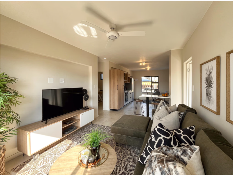 Open-plan living area featuring tiled flooring, a ceiling fan, and a seamless transition into a modern kitchen with built-in cabinetry.