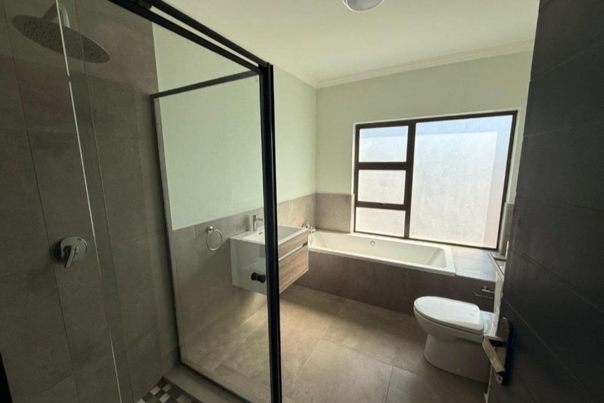 Modern bathroom featuring a glass-enclosed walk-in shower, a built-in bathtub, a wall-mounted vanity, and a toilet with neutral floor-to-ceiling tiling.