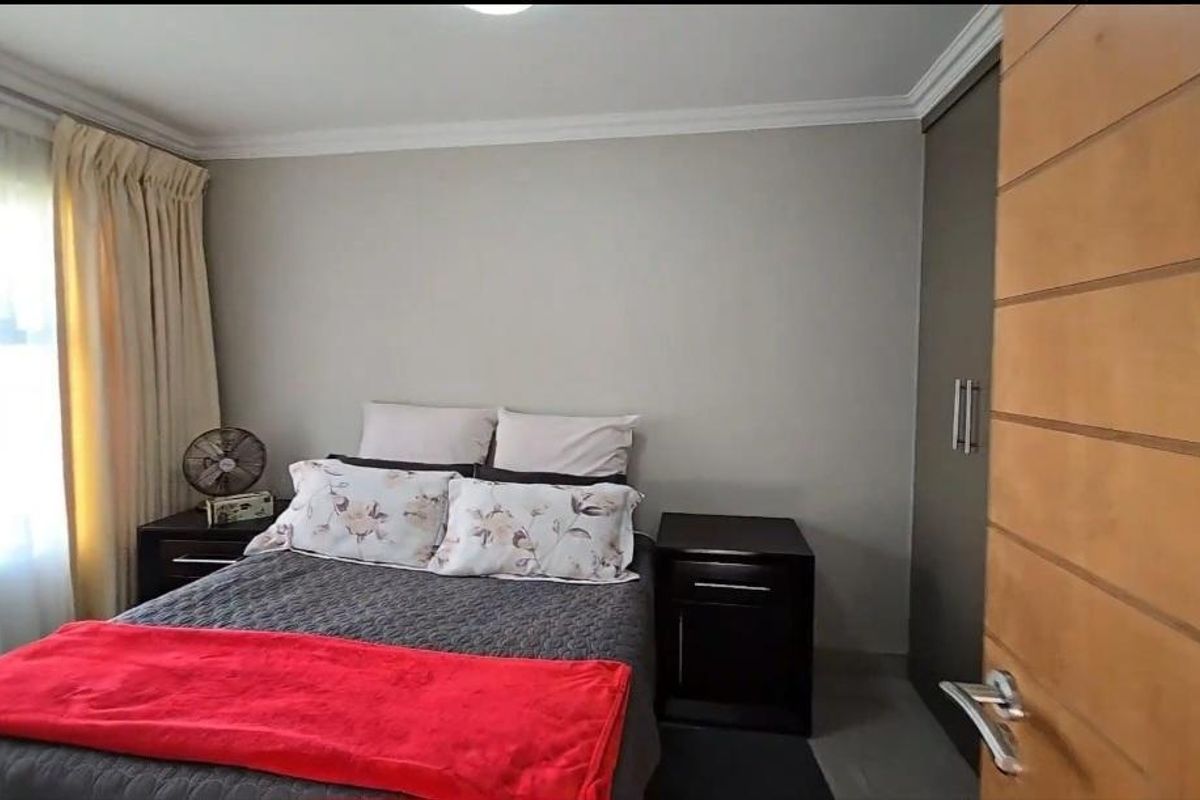 A well-maintained bedroom featuring built-in cupboards, neutral wall finishes, and a large window allowing for natural light.