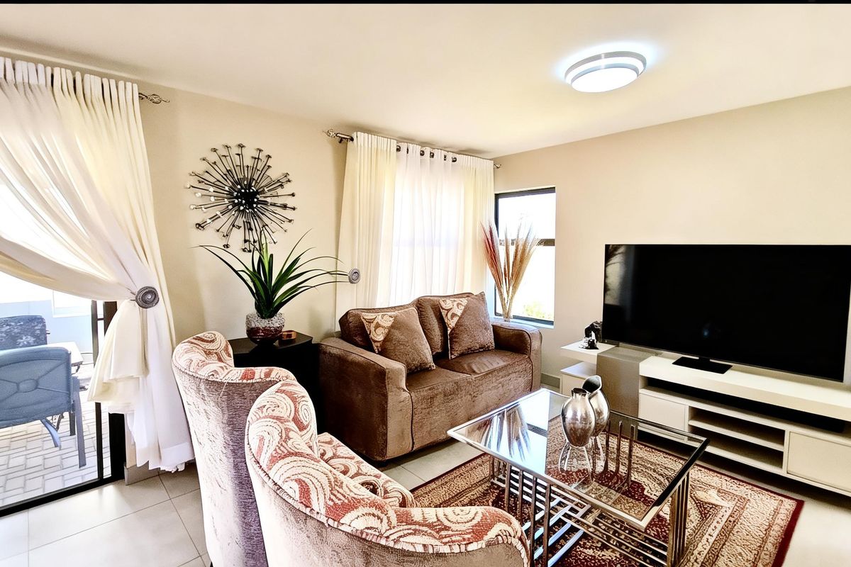 A well-maintained living room featuring tiled flooring, large windows with curtains, and direct access to an outdoor patio area.