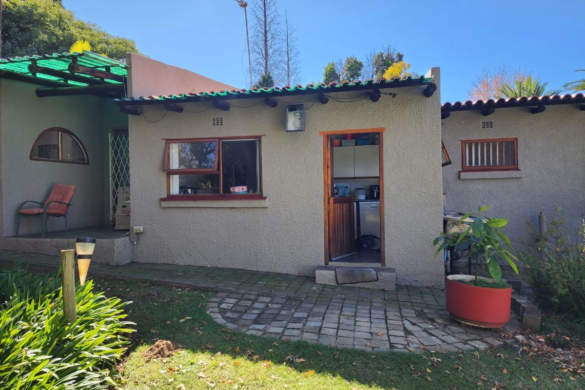 Rear exterior view of the property featuring a paved patio area, textured wall finish, and access to the kitchen through a timber door.