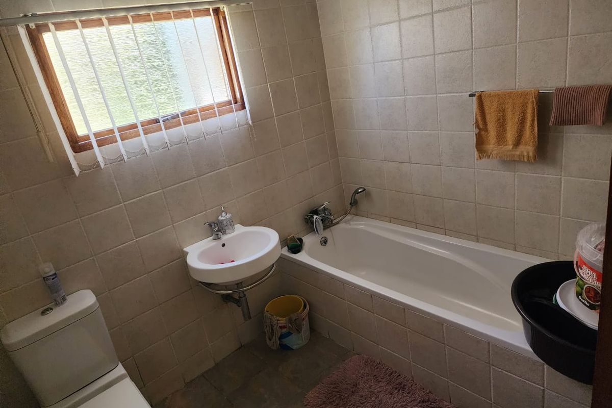 A functional bathroom featuring a built-in bathtub, wall-mounted basin, and toilet with neutral wall tiling and a window for natural light.