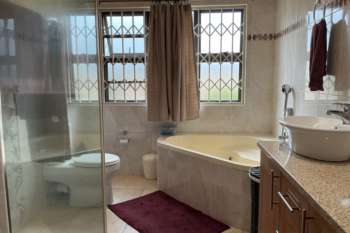 A functional bathroom featuring a corner bathtub, glass-enclosed shower, vessel sink vanity with granite countertop, and tiled finishes throughout.