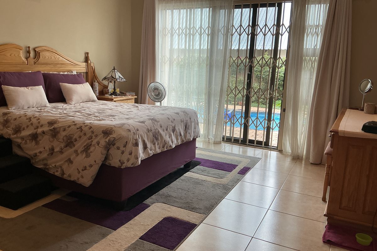 Spacious bedroom featuring tiled flooring and a sliding glass door with security gate, providing direct access to the outdoor pool area.