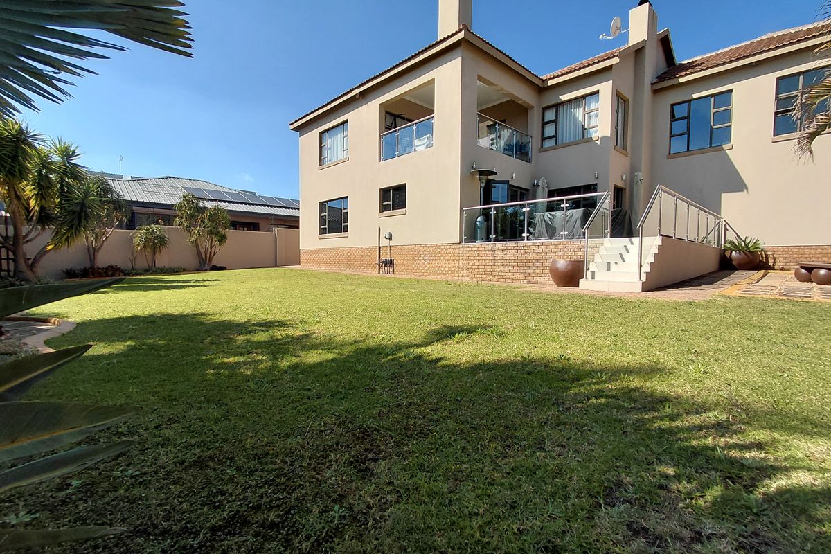 A spacious rear garden featuring a well-maintained lawn, leading to a multi-level house with a covered patio and balcony with glass balustrades.