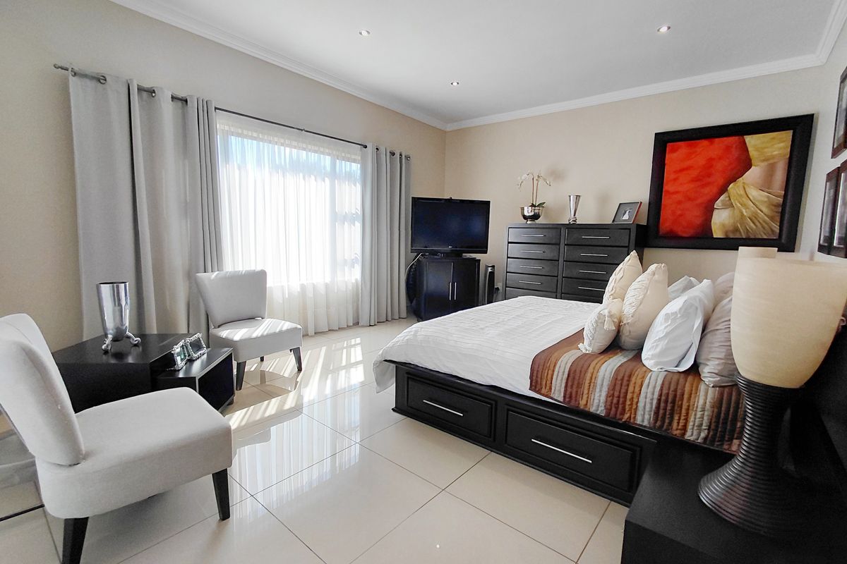 Spacious bedroom featuring polished porcelain floor tiles, recessed downlighting, and large windows with integrated curtain tracks.