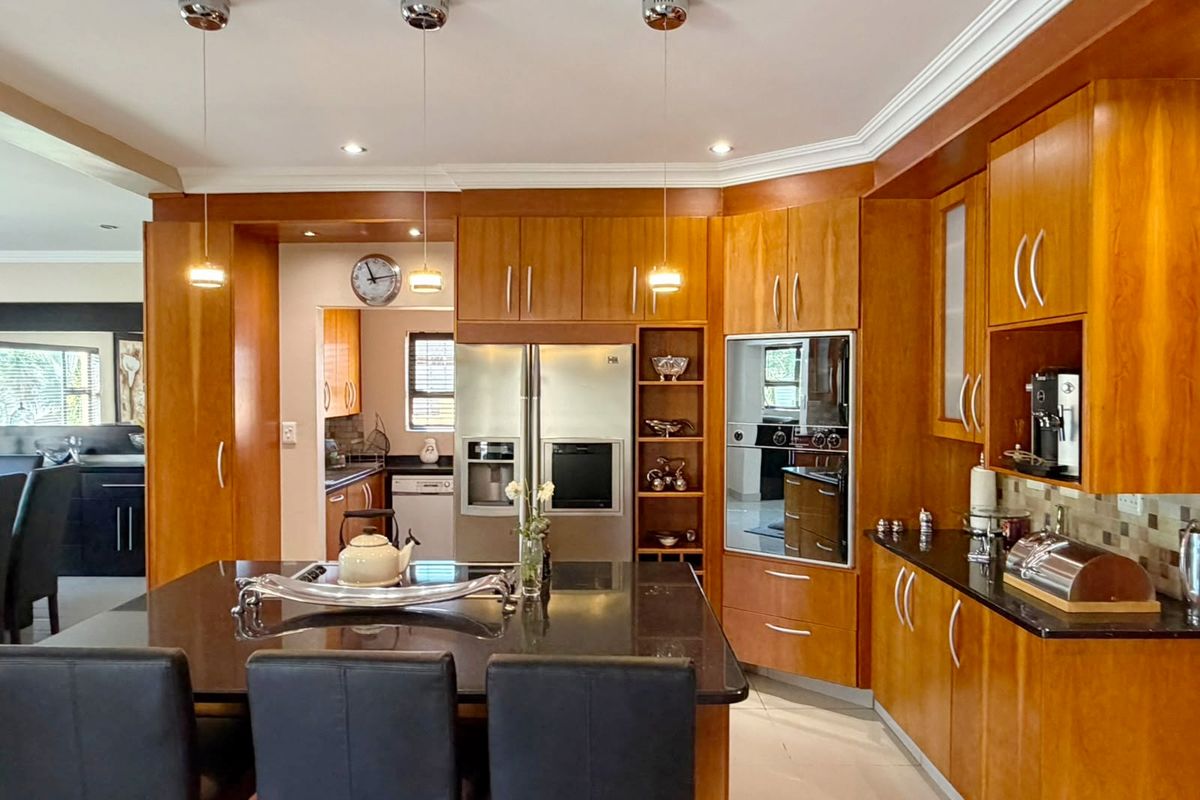 A well-appointed kitchen featuring warm-toned wooden cabinetry, a large central island with a dark stone countertop, and integrated stainless steel appliances.