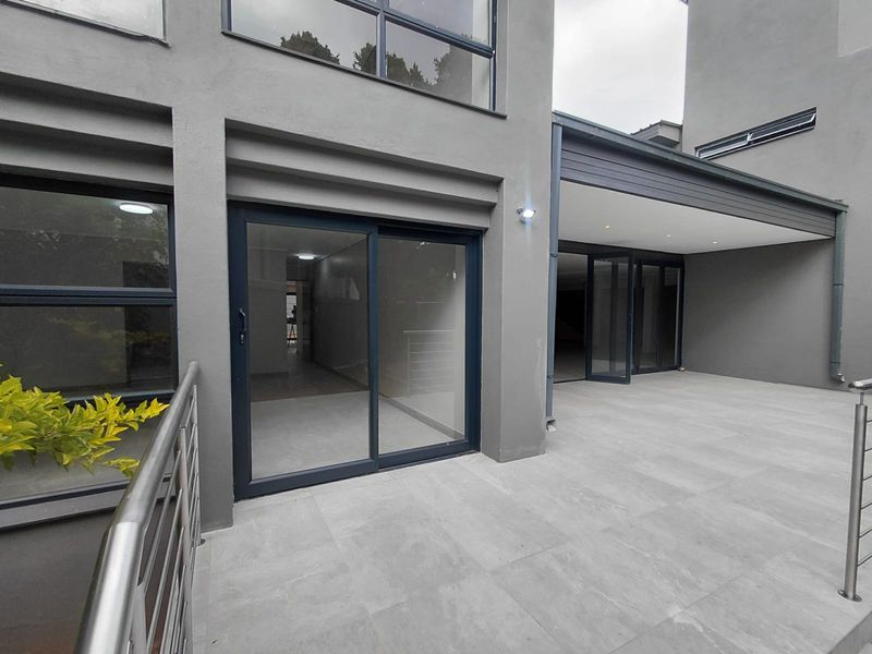 A modern, spacious covered patio featuring large-format floor tiles, sleek sliding glass doors, and a contemporary stainless steel balustrade.