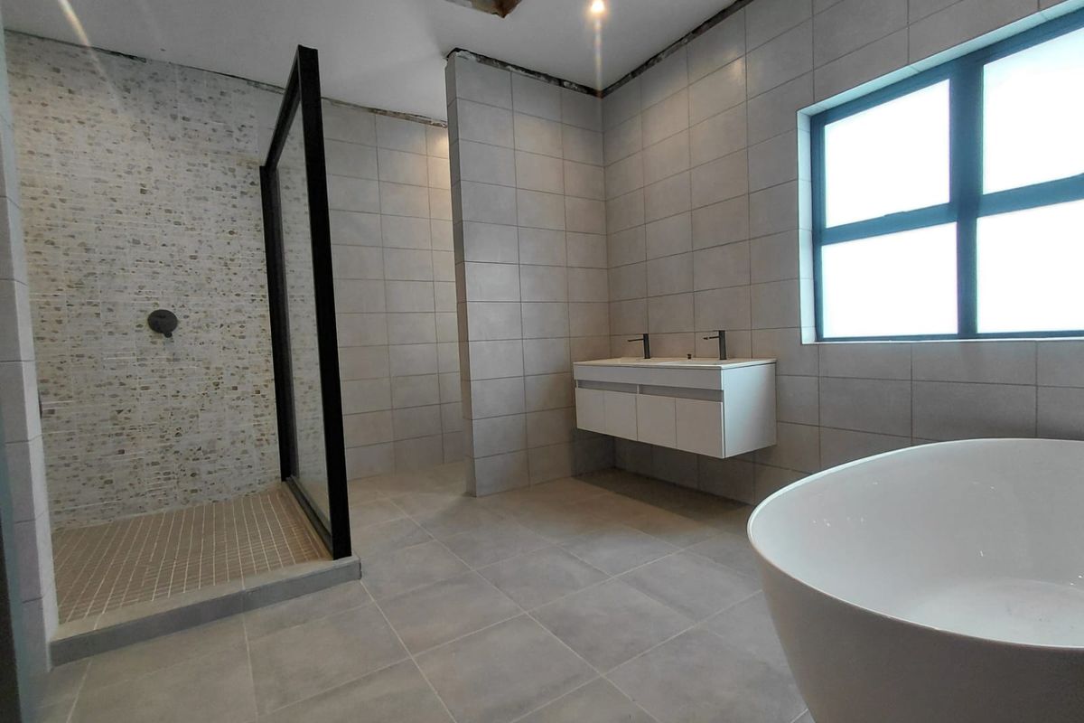 Modern bathroom featuring a walk-in shower, freestanding bathtub, and wall-mounted double vanity, currently requiring final ceiling finishing touches.