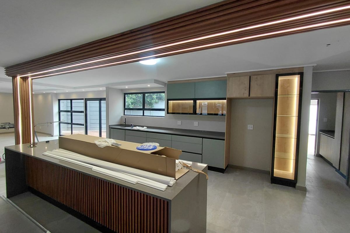 Modern, newly installed kitchen featuring a large island with slatted timber detailing, stone countertops, integrated cabinetry, and ambient LED lighting.
