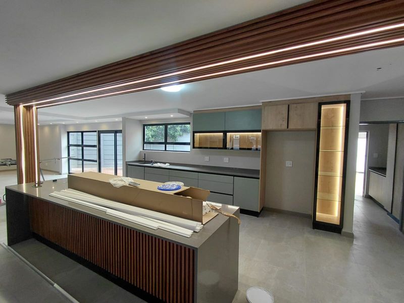 Modern, newly installed kitchen featuring a large island with slatted timber detailing, stone countertops, integrated cabinetry, and ambient LED lighting.