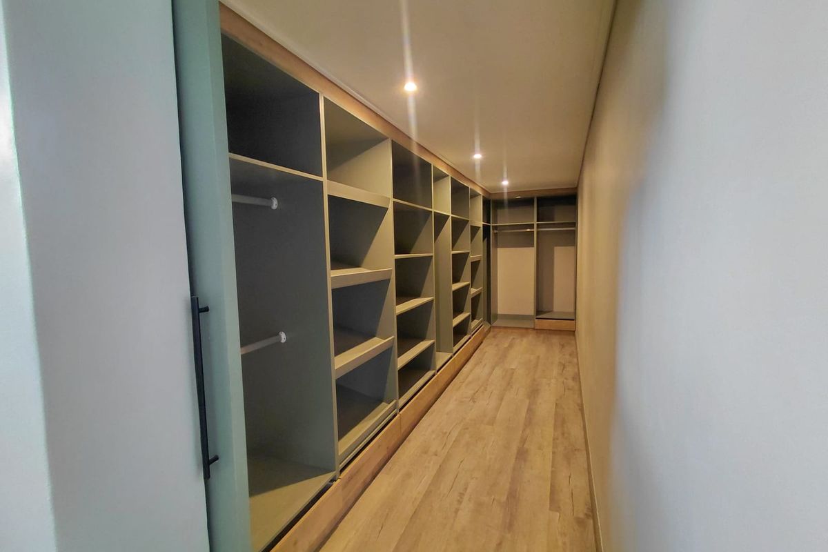 A spacious walk-in closet featuring extensive built-in shelving, hanging rails, modern recessed lighting, and durable laminate flooring.