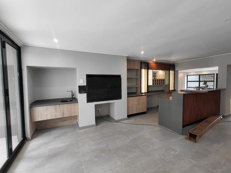 Modern open-plan entertainment area featuring a built-in braai, custom cabinetry, bar counter, and large sliding doors leading to the exterior.
