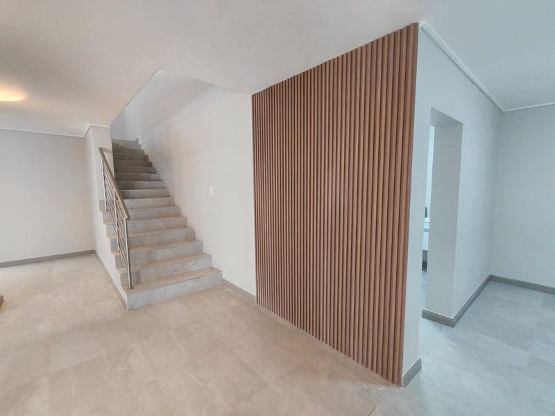 Modern entrance area featuring a staircase with metal balustrade and a decorative slatted timber feature wall, finished with neutral floor tiles.