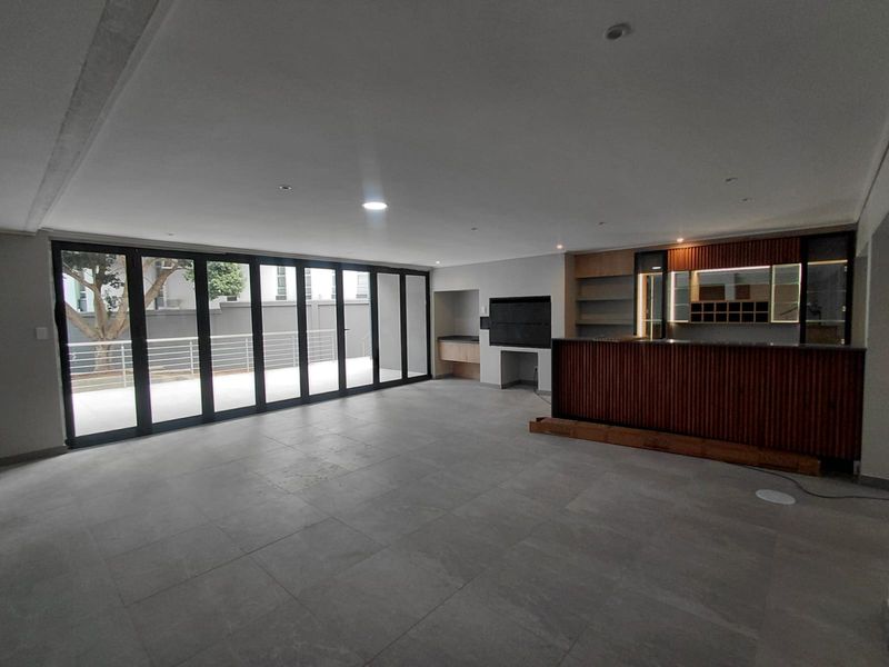 Spacious open-plan living area featuring a built-in bar, indoor braai, and large stacking doors leading to an outdoor patio.