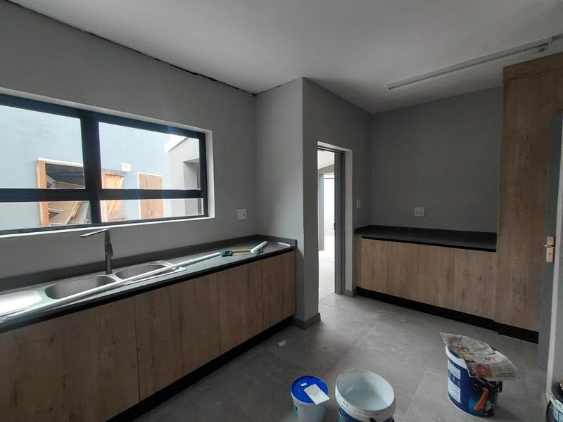 A modern, newly installed kitchen featuring wood-look cabinetry, dark countertops, and tiled flooring, currently in the final stages of completion.