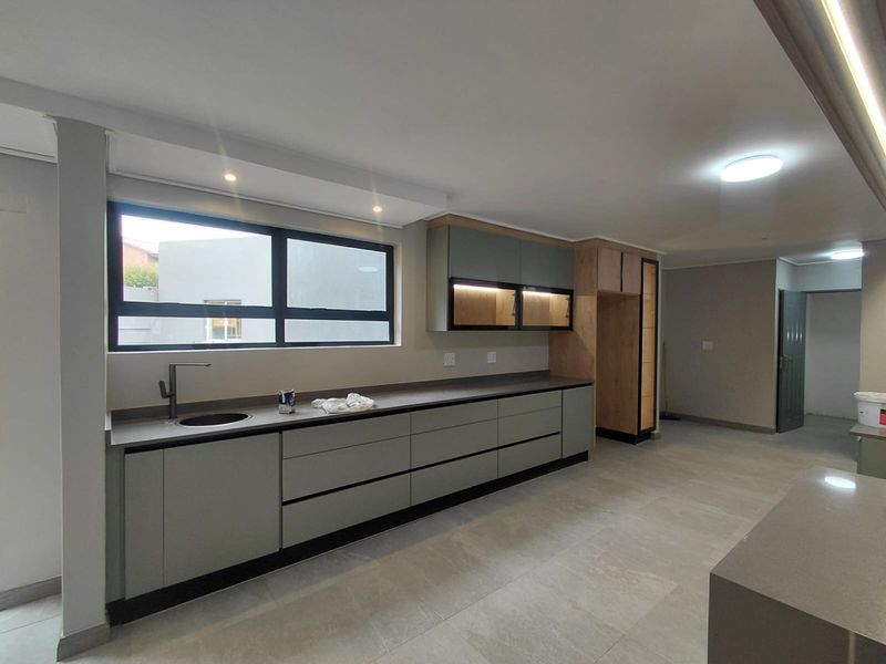 Modern kitchen featuring sleek grey cabinetry, stone countertops, integrated lighting, and large format floor tiles in a clean, contemporary open-plan space.