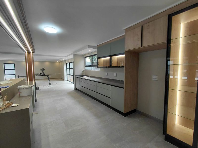 Modern, newly renovated kitchen featuring sleek cabinetry, stone countertops, integrated lighting, and large format floor tiles in an open-plan layout.