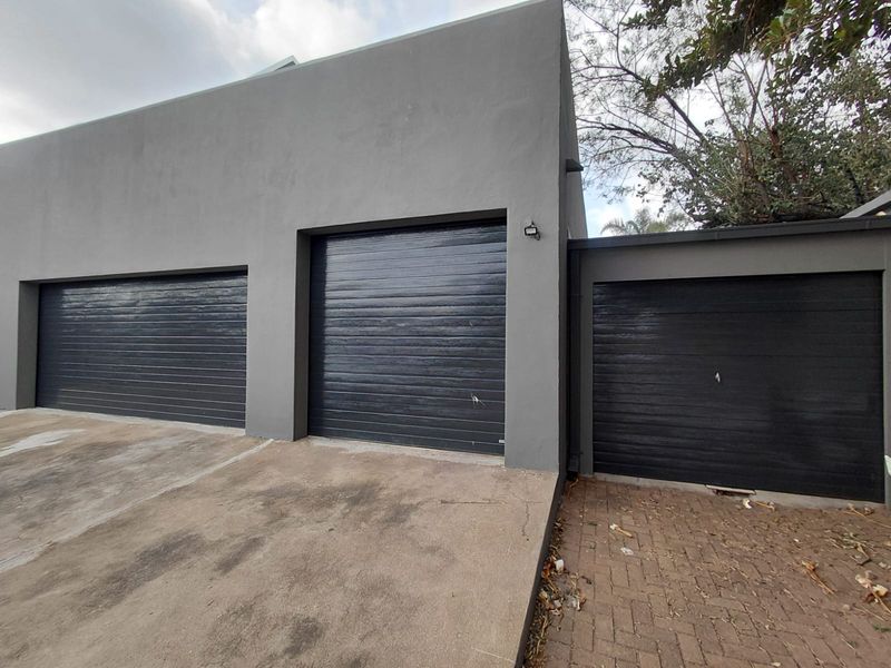 A modern triple garage featuring dark grey sectional doors and a combination of concrete and paved driveway surfaces.