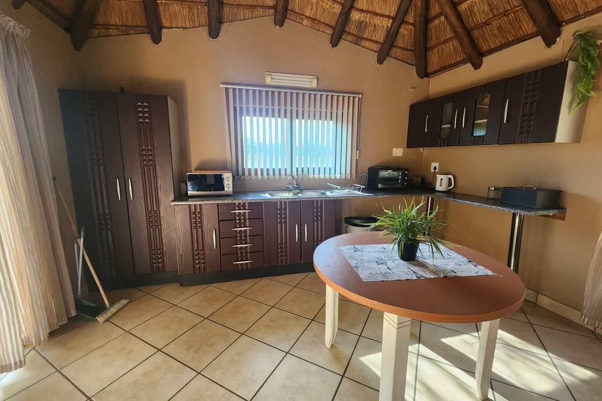 A rustic kitchen featuring dark wood cabinetry, tiled flooring, and a traditional thatched roof ceiling, creating a warm and unique farm-style atmosphere.