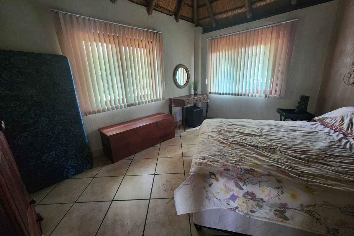 A bedroom featuring a traditional thatched roof, tiled flooring, and vertical blinds on the windows.
