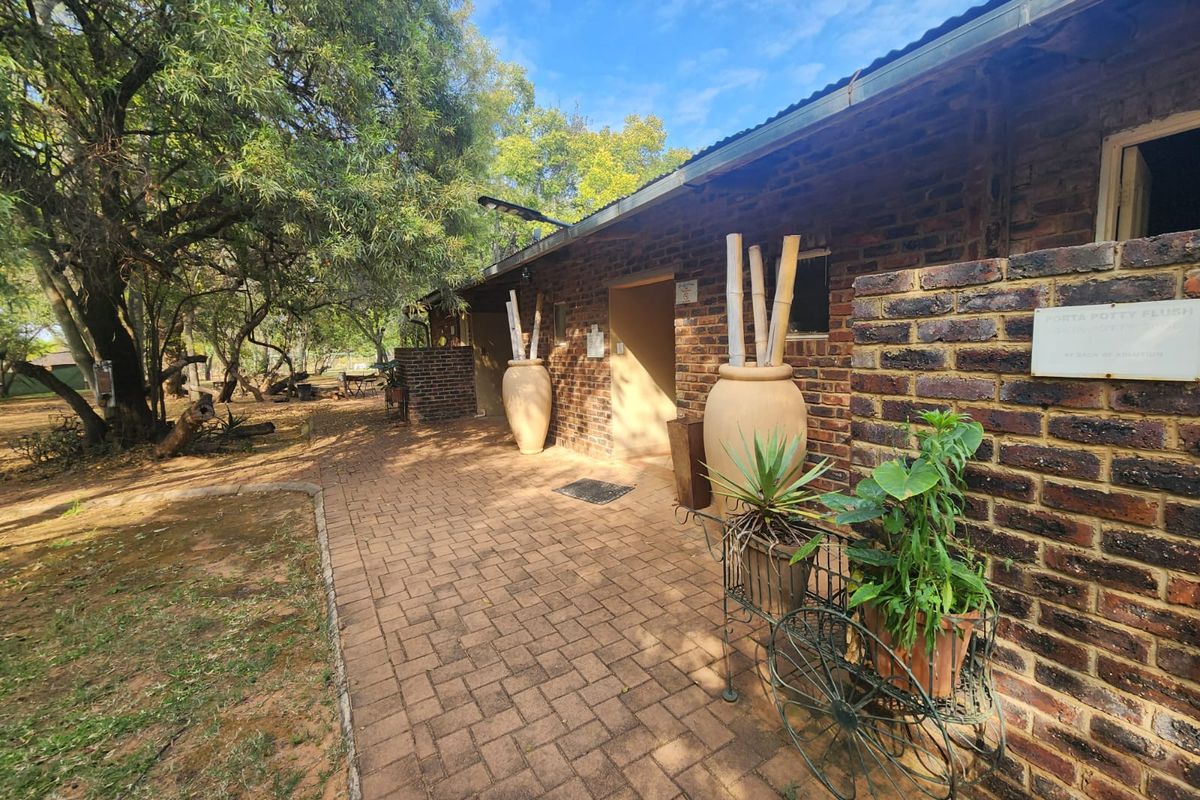 Exterior view of a rustic brick farm building featuring a paved walkway and mature trees in a natural garden setting.