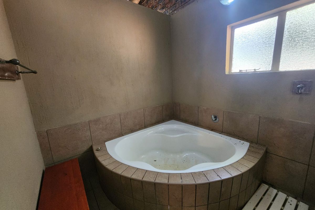 A bathroom featuring a built-in corner bathtub with tiled surround and a small window, requiring maintenance and cleaning.