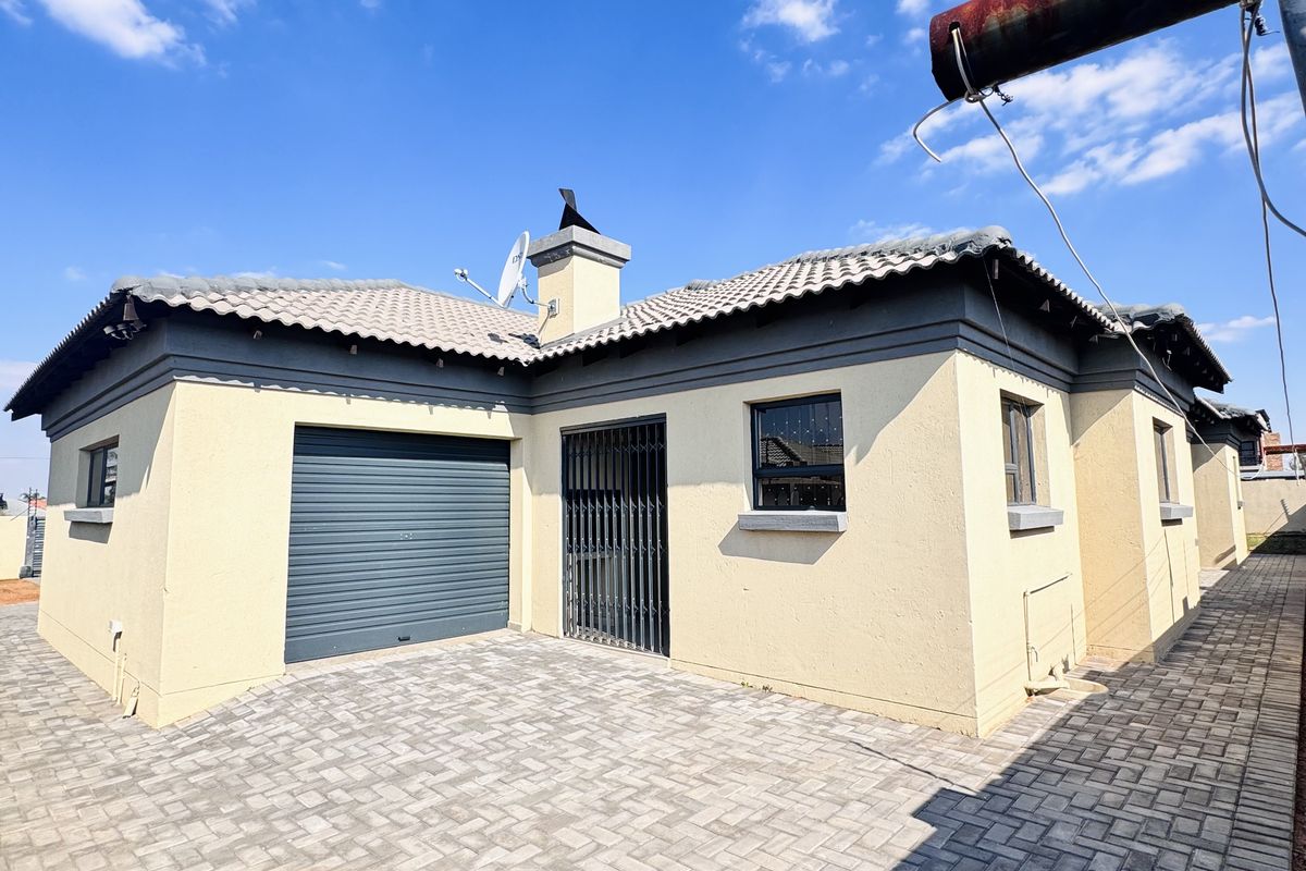 Rear view of the property featuring a paved courtyard, a single garage with a roller door, and security gates on the entrance.