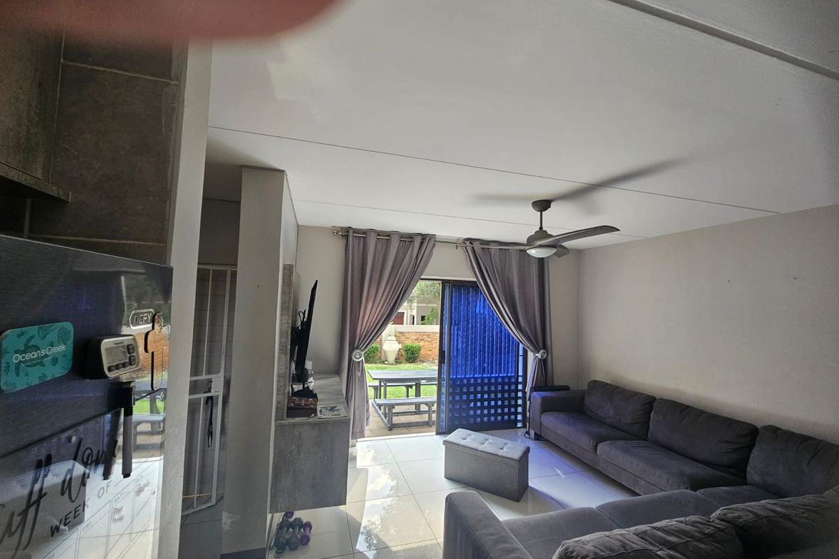 Open-plan living area featuring tiled floors, a ceiling fan, and a sliding glass door providing direct access to the rear patio and garden.