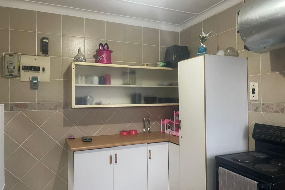 A compact kitchen area featuring basic cabinetry, tiled walls, and a built-in stove, requiring cosmetic updates to modernize the space.