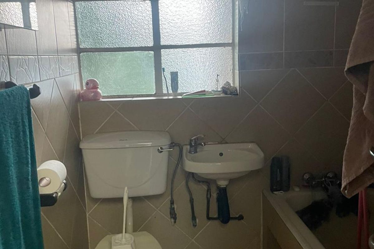 A compact, dated bathroom featuring a standard toilet, wall-mounted basin, and a bathtub with tiled walls and flooring.