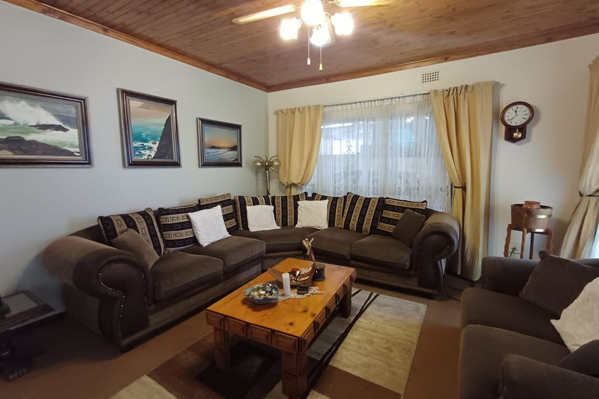 A comfortable living room featuring a warm timber-clad ceiling, neutral walls, and large windows with classic drapery.