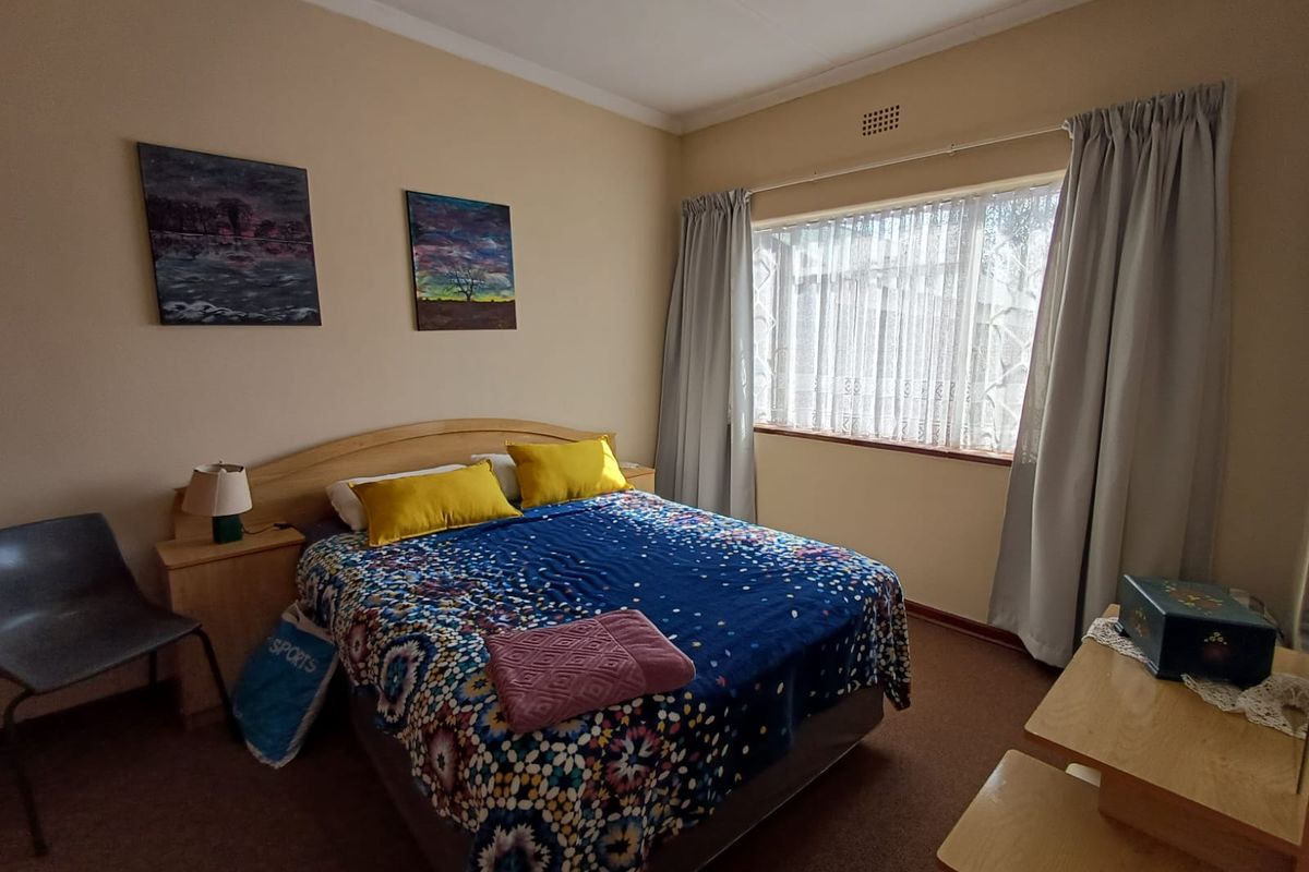 A standard bedroom featuring carpeted flooring, a large window with curtain tracks, and a ceiling ventilation vent.