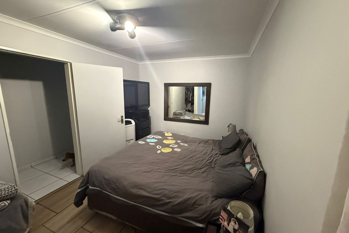 A standard bedroom featuring tiled flooring, a ceiling-mounted light fixture, and an adjoining doorway leading to a tiled utility or bathroom area.