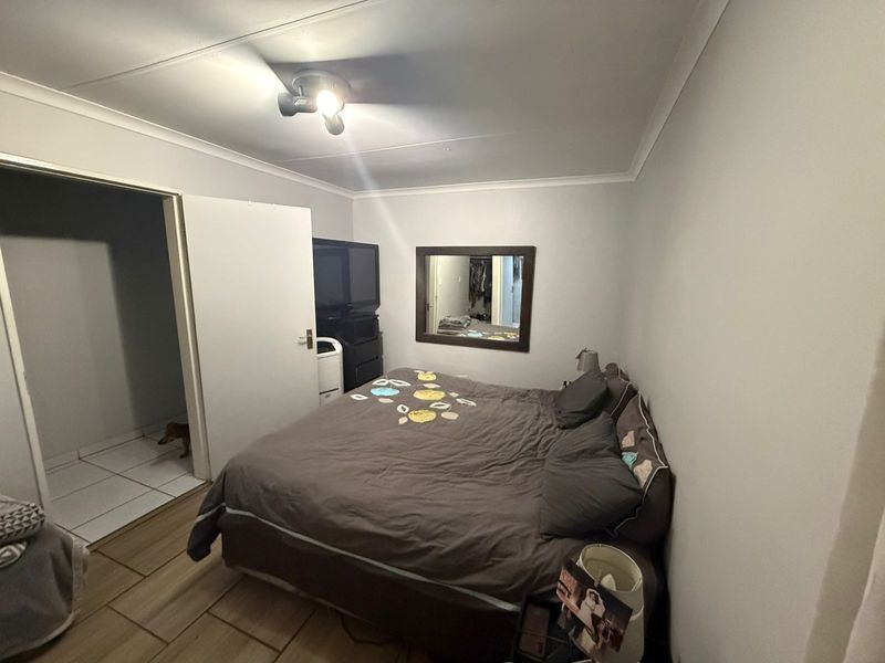 A standard bedroom featuring tiled flooring, a ceiling-mounted light fixture, and an adjoining doorway leading to a tiled utility or bathroom area.