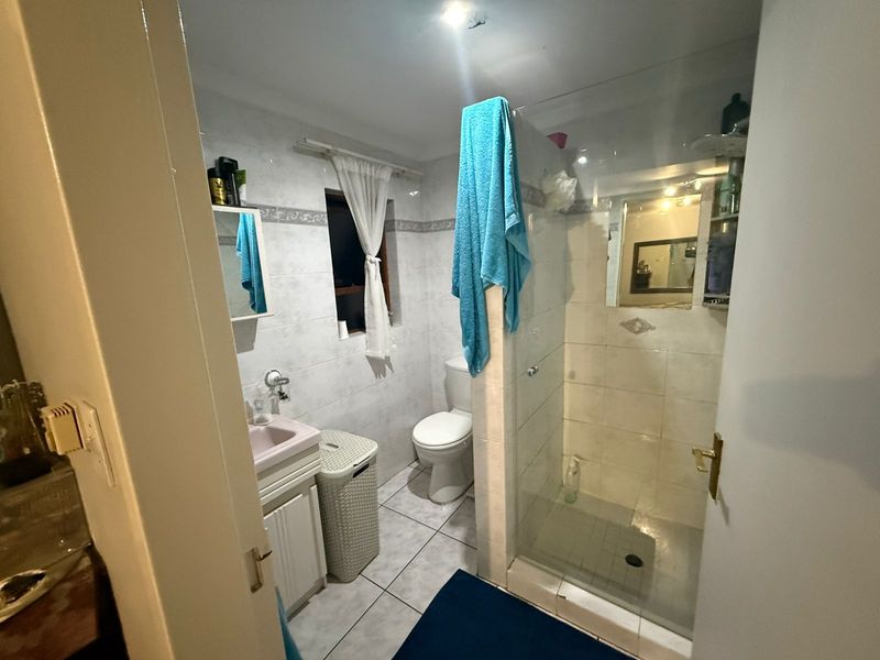 A functional bathroom featuring a glass-enclosed shower, vanity basin, and toilet with tiled walls and flooring.
