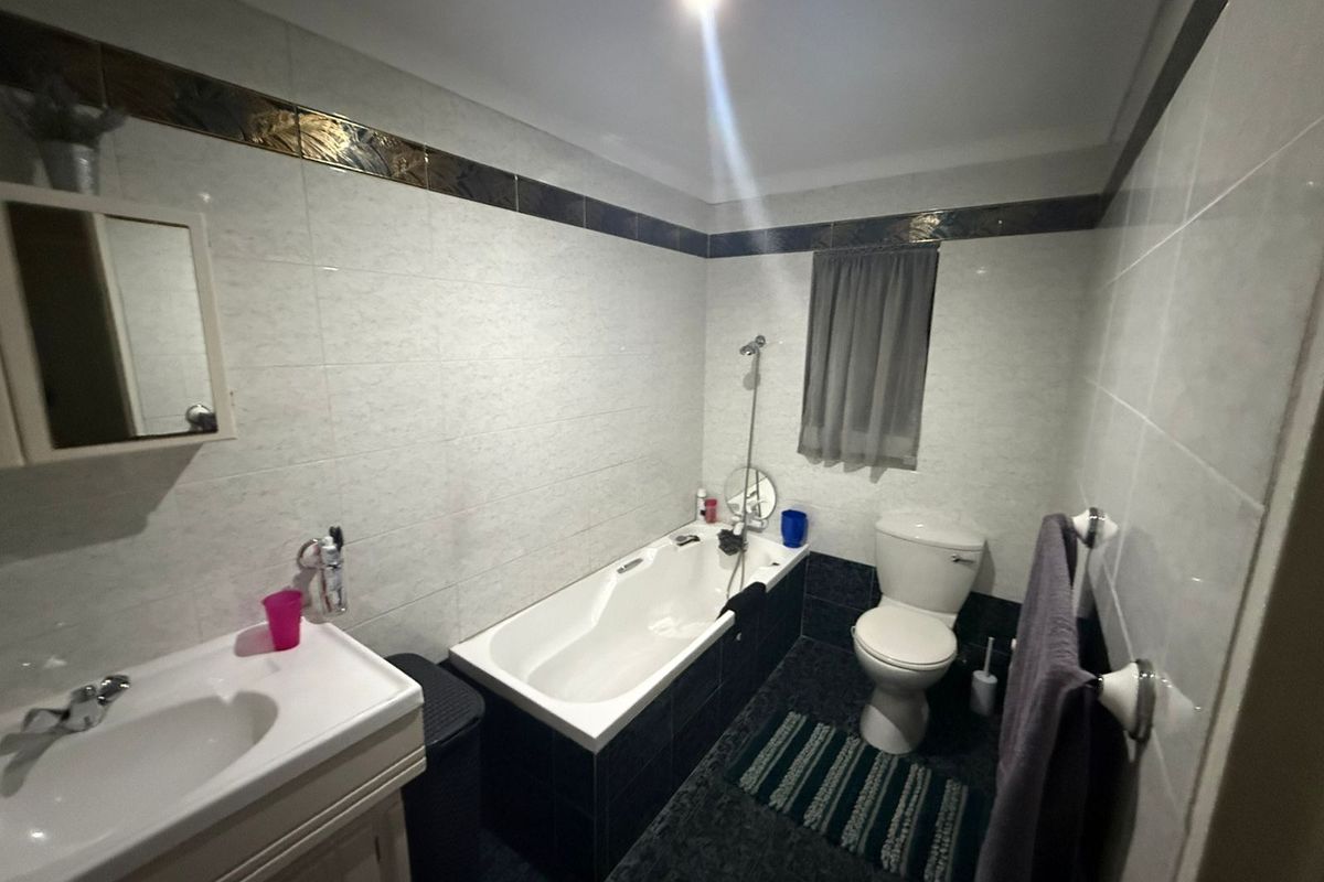 A functional bathroom featuring a built-in bathtub, a pedestal vanity with a basin, and a standard toilet, finished with tiled walls and flooring.