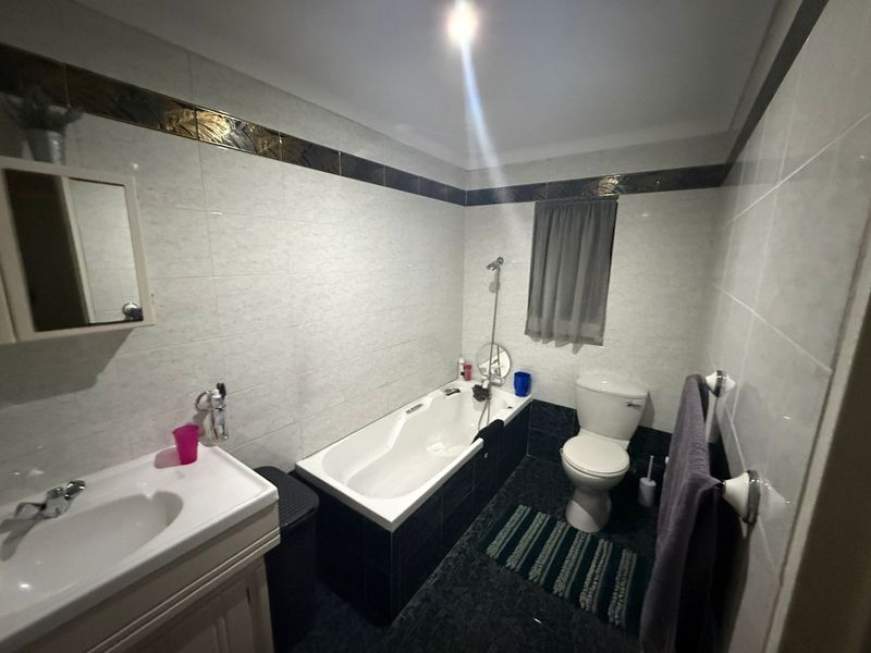 A functional bathroom featuring a built-in bathtub, a pedestal vanity with a basin, and a standard toilet, finished with tiled walls and flooring.